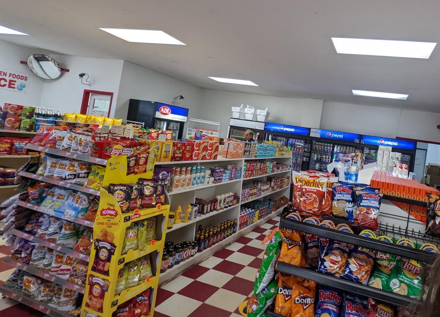 Store aisles stocked with chips, snacks and groceries, with drink coolers at the back